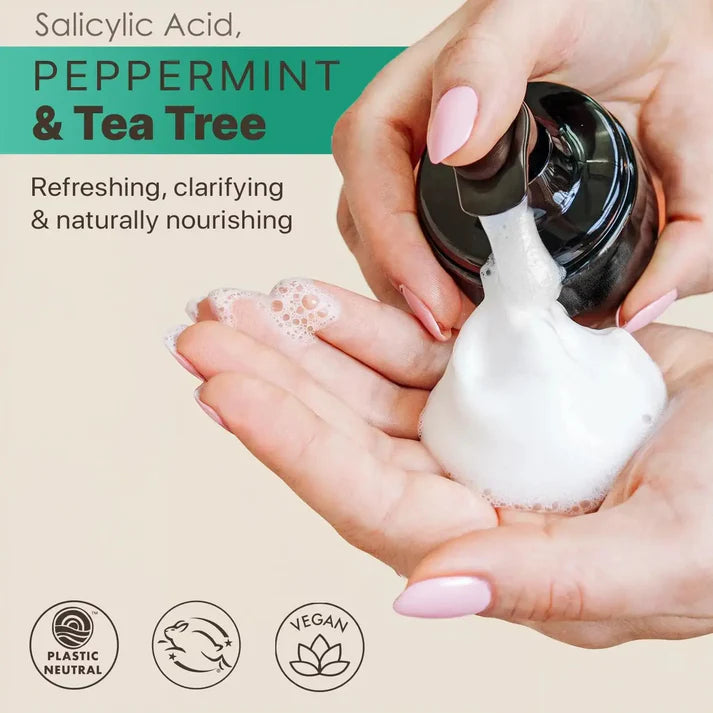 Hands holding a bottle of foamy product with salicylic acid, peppermint, and tea tree ingredients.